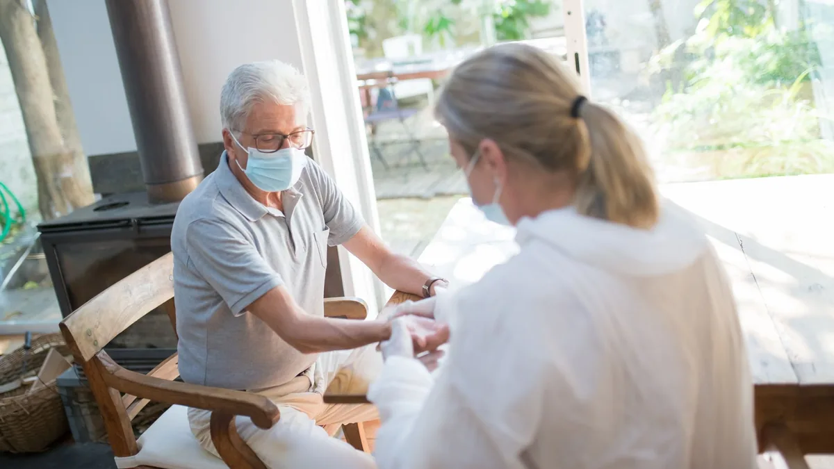 A healthcare worker examining a senior man at home with face masks during the pandemic.