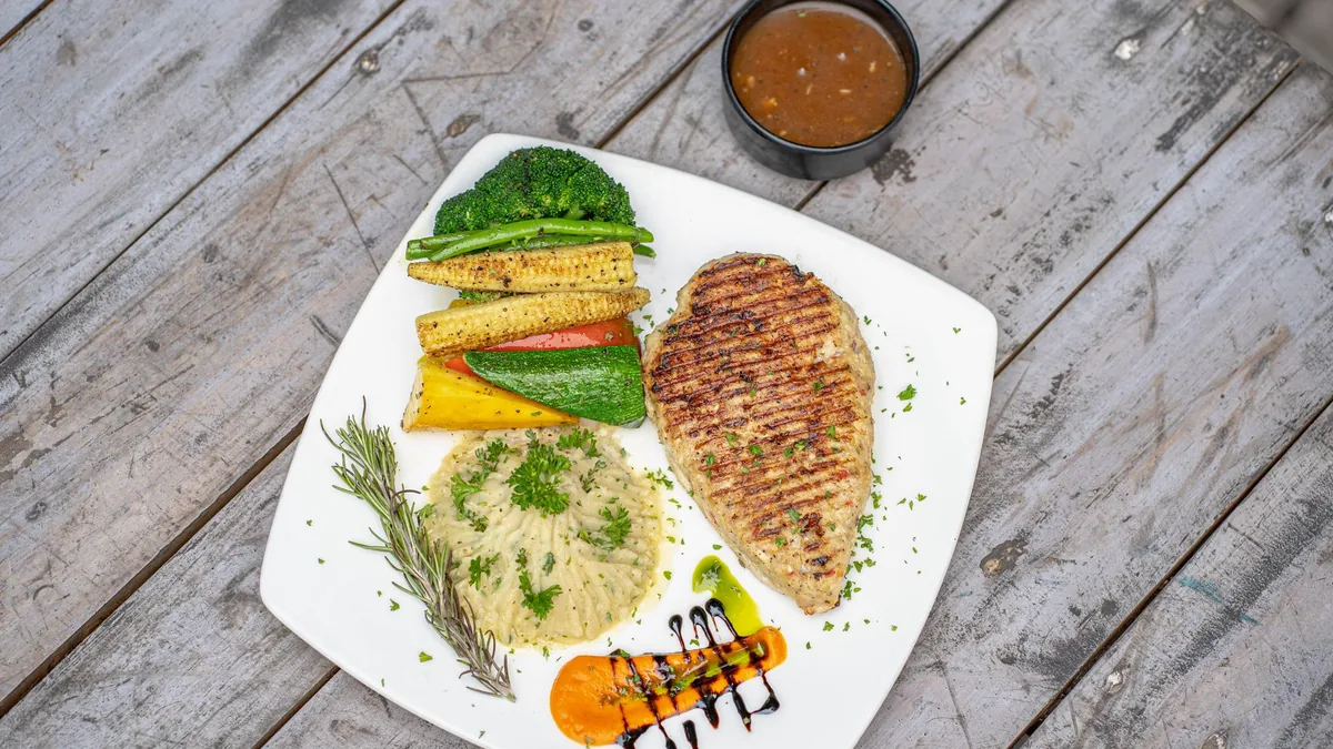 Grilled chicken and vegetables elegantly plated on a rustic table.