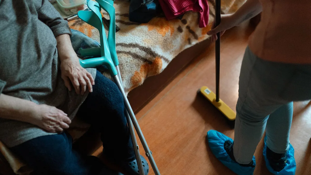 Caregiver helps an elderly woman with cleaning tasks.